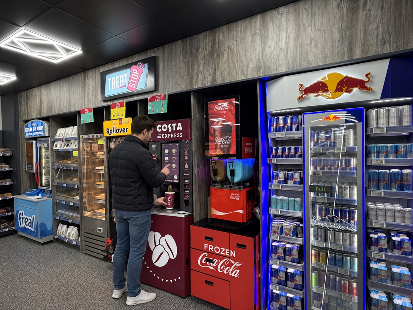 A customer at the in-store Treat Stop, using the Costa Express coffee machine alongside frozen drinks and chilled drinks fixtures at an NTS site.